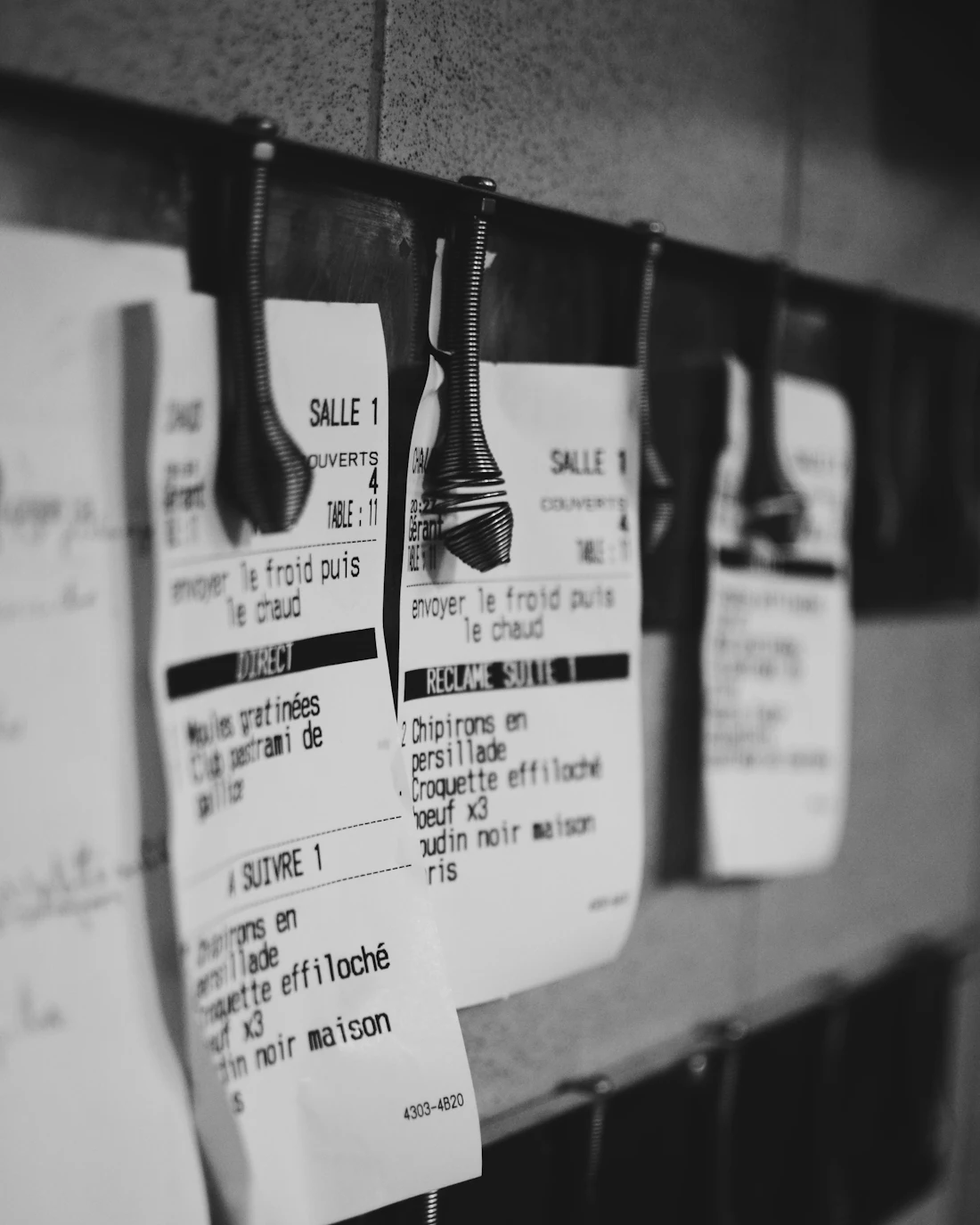 Order tickets clipped to the rail at a restaurant kitchen pass during service.